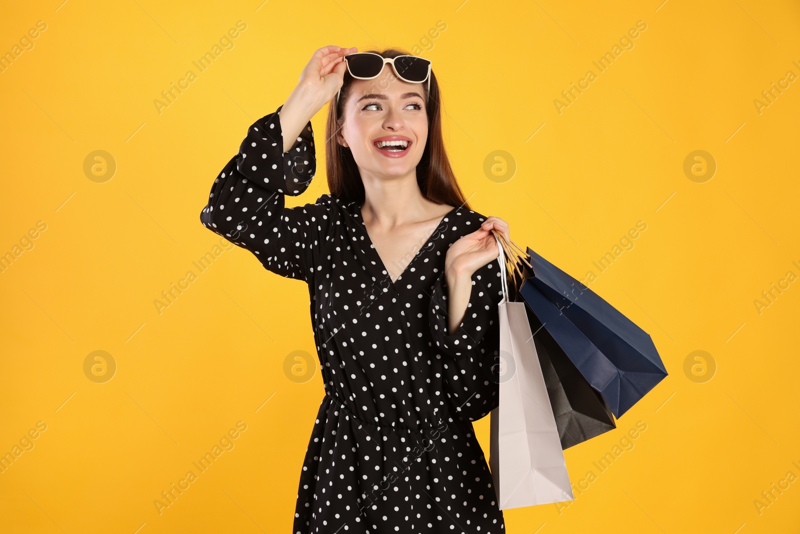 Photo of Happy young woman with shopping bags on yellow background. Big sale