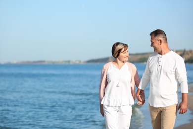 Happy mature couple walking at beach on sunny day