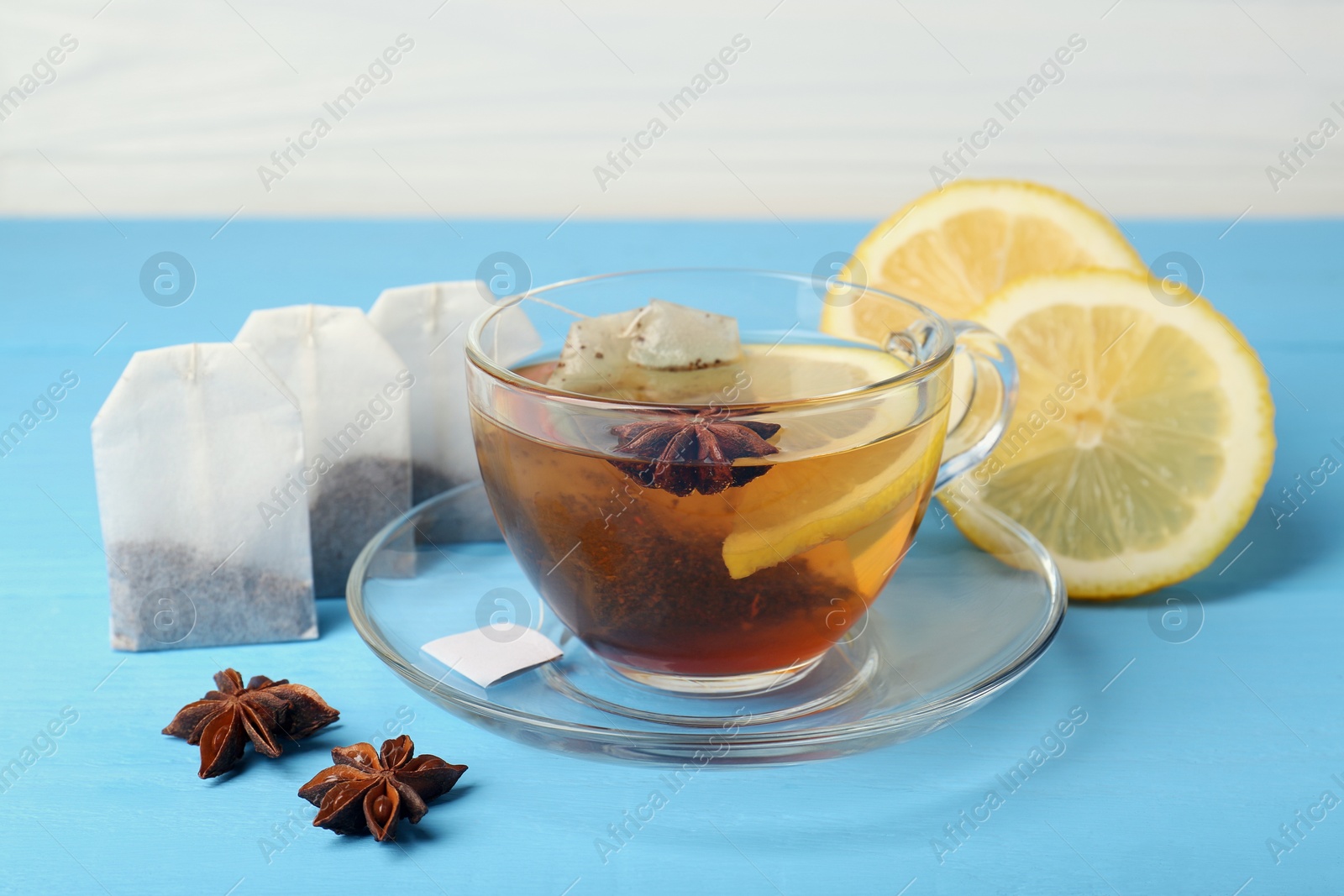 Photo of Tea bags, cup of hot drink, anise stars and lemon on light blue wooden table