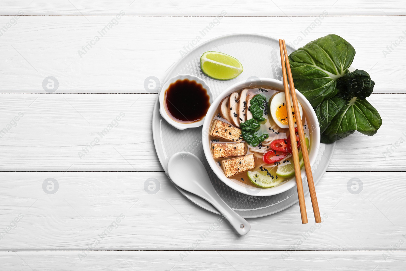 Photo of Delicious vegetarian ramen, soy sauce and pak choy leaves on white wooden table, top view. Space for text