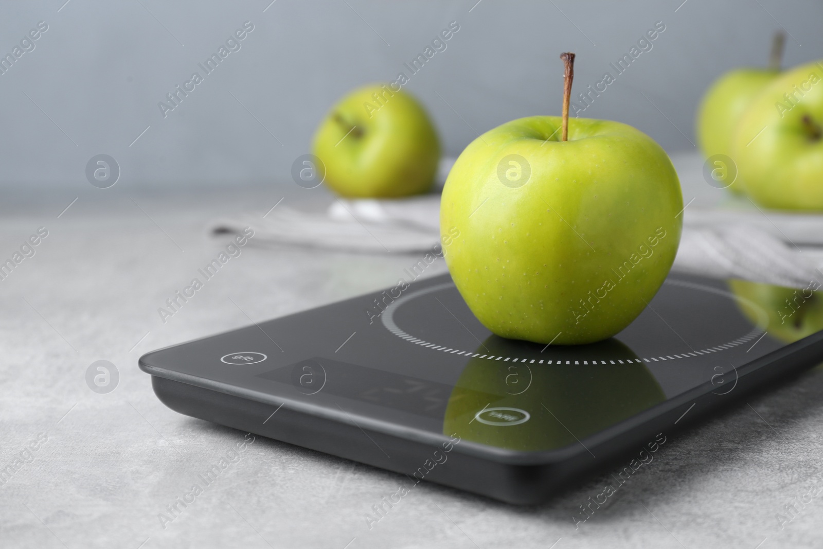 Photo of Digital kitchen scale with ripe green apple on grey table