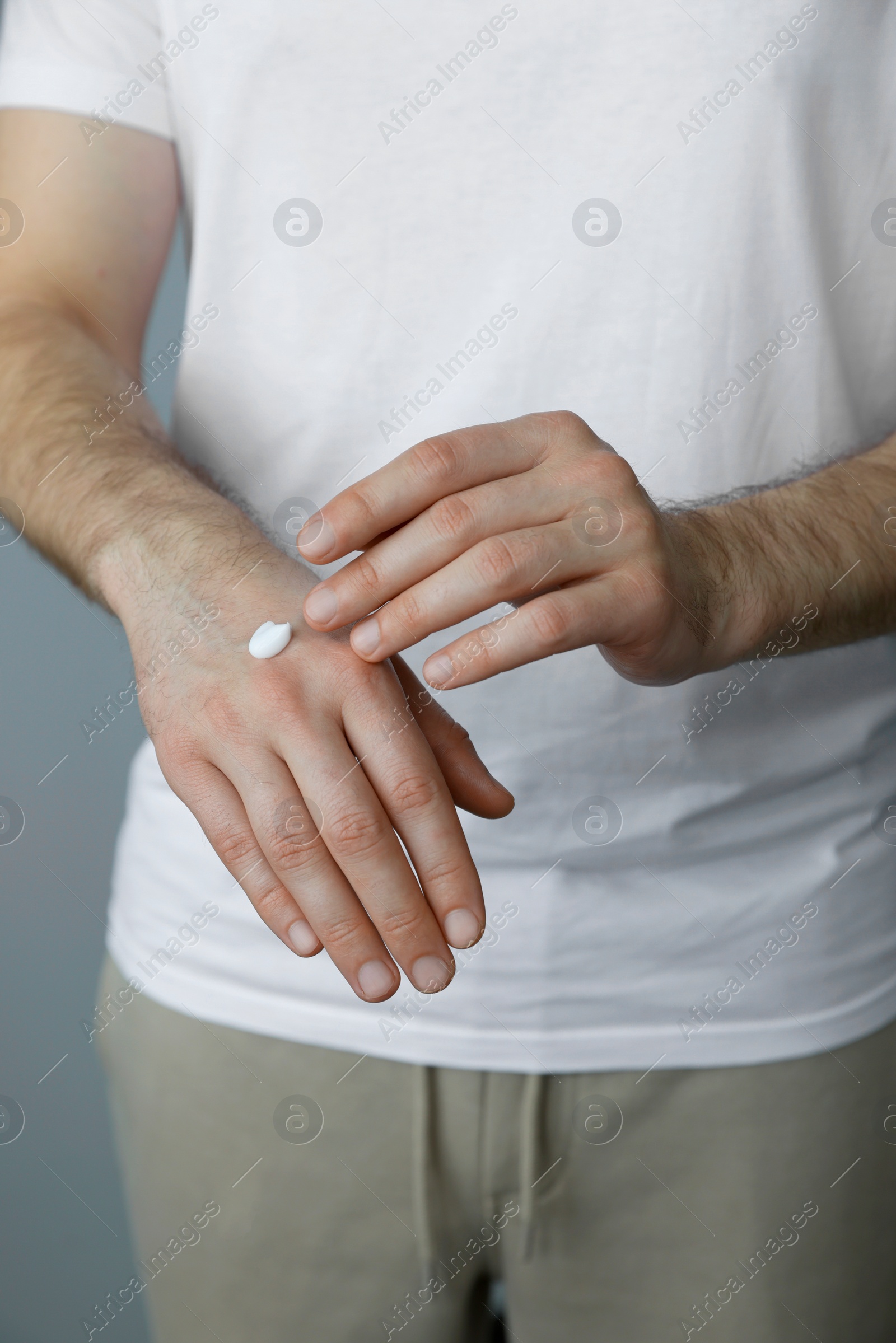 Photo of Man applying cream onto hand against grey background, closeup