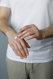 Photo of Man applying cream onto hand against grey background, closeup