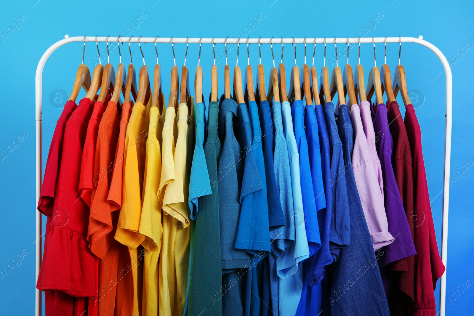 Photo of Rack with bright clothes on blue background. Rainbow colors