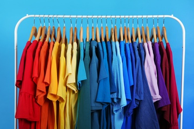 Photo of Rack with bright clothes on blue background. Rainbow colors