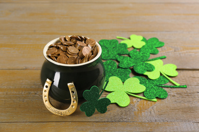 Photo of Pot of gold coins, horseshoe and clover leaves on wooden table. St. Patrick's Day celebration