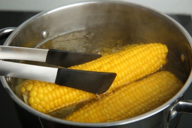 Photo of Taking fresh corn cob from pot with hot water on stove