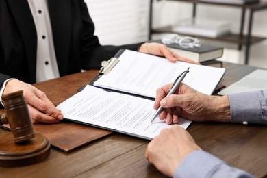 Photo of Senior man signing document in lawyer's office, closeup