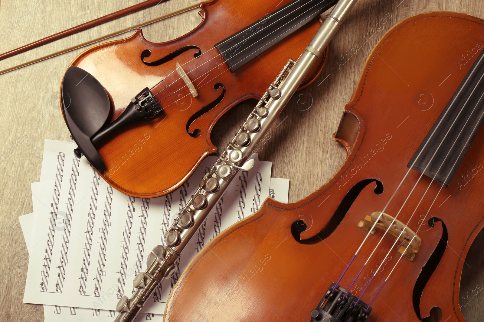 Photo of Violin, violoncello, flute and note sheets on wooden background, flat lay. Musical instruments