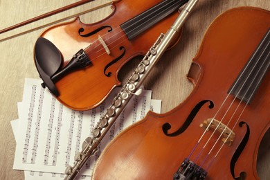 Photo of Violin, violoncello, flute and note sheets on wooden background, flat lay. Musical instruments