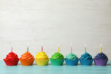 Photo of Delicious birthday cupcakes with burning candles on blue wooden table