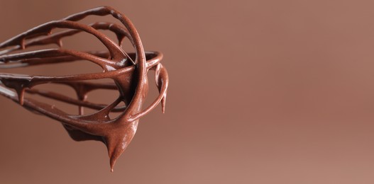 Image of Whisk with yummy chocolate cream on light brown background, closeup. Banner design with space for text