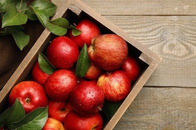 Crate with wet red apples and green leaves on wooden table, top view