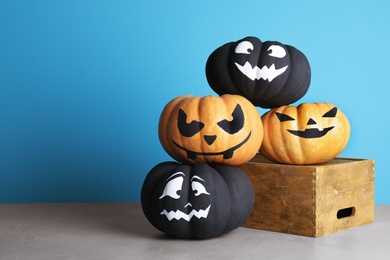 Photo of Pumpkins with scary faces on table against color background, space for text. Halloween decor