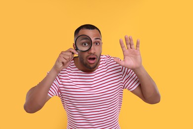 Photo of Shocked man looking through magnifier glass on orange background