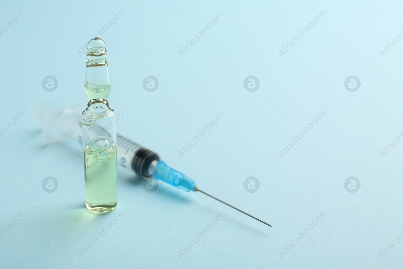 Photo of Glass ampoule with liquid and syringe on light blue background. Space for text