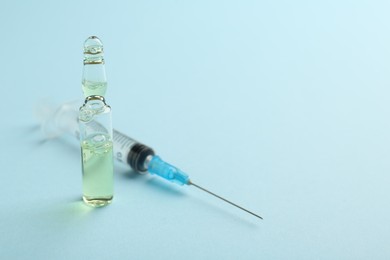 Photo of Glass ampoule with liquid and syringe on light blue background. Space for text