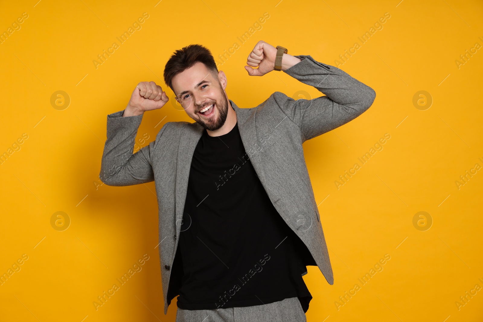 Photo of Handsome man in stylish grey jacket celebrating victory on yellow background