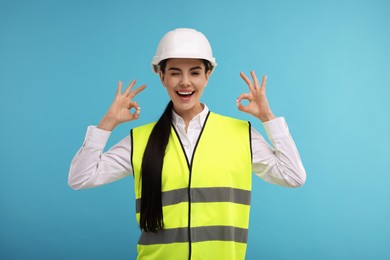 Engineer in hard hat showing ok gesture on light blue background