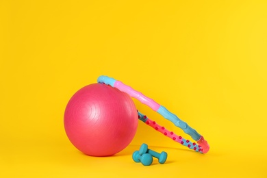 Photo of Hula hoop, exercise ball and dumbbells on yellow background