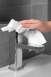 Photo of Woman cleaning faucet of bathroom sink with paper towel, closeup