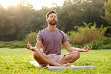 Man practicing yoga on mat outdoors. Lotus pose