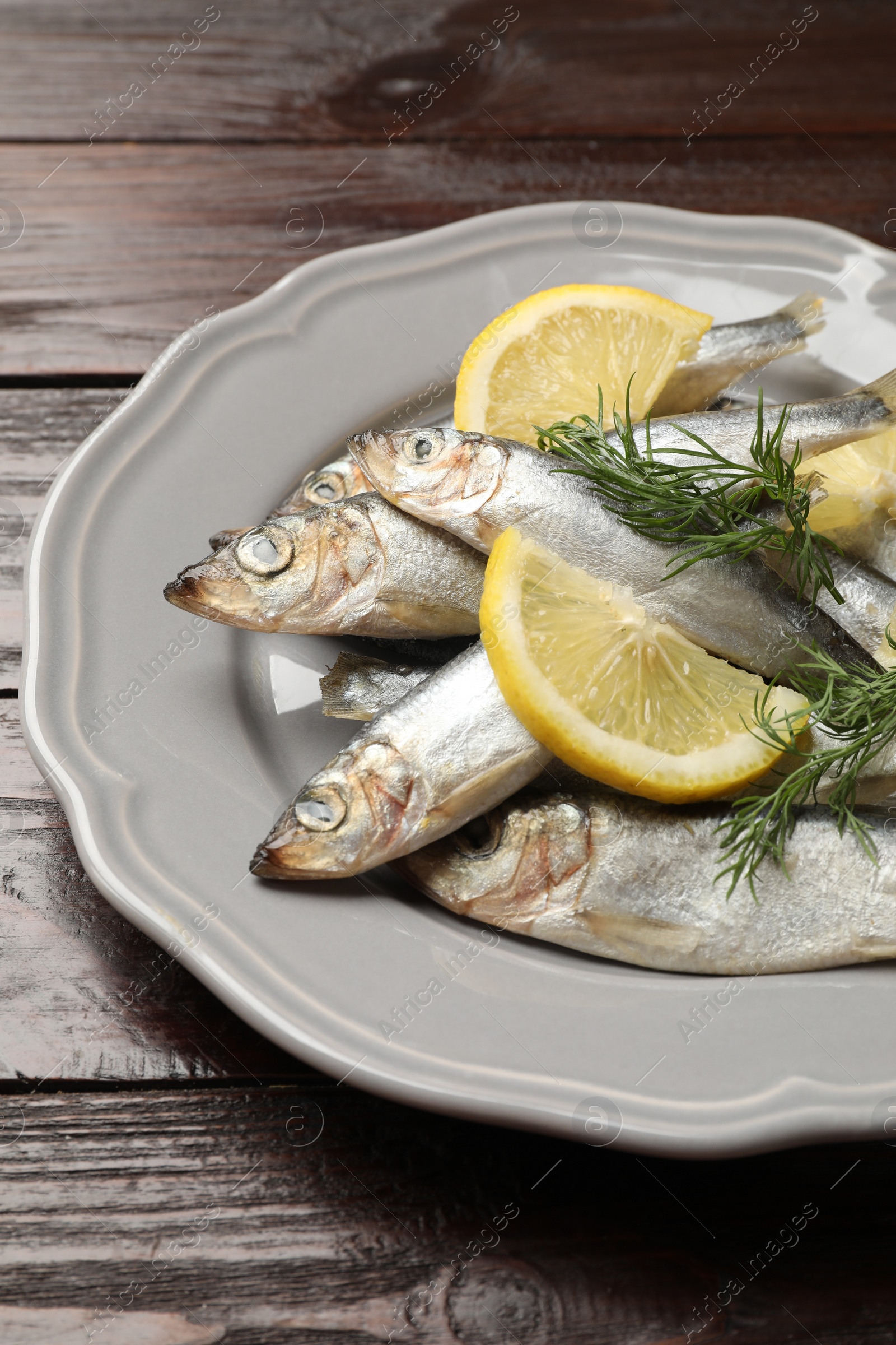 Photo of Fresh raw sprats, dill and cut lemon on wooden table