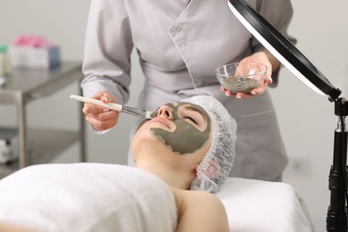 Photo of Cosmetologist applying mask on woman's face in clinic, closeup