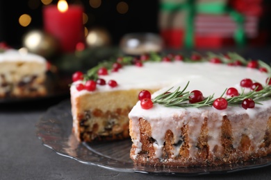 Photo of Traditional Christmas cake decorated with rosemary and cranberries on black table, closeup