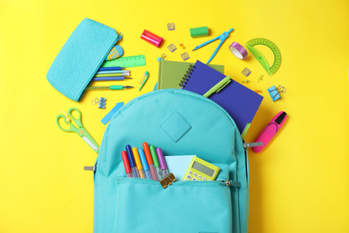 Photo of Stylish backpack with different school stationery on yellow background, flat lay