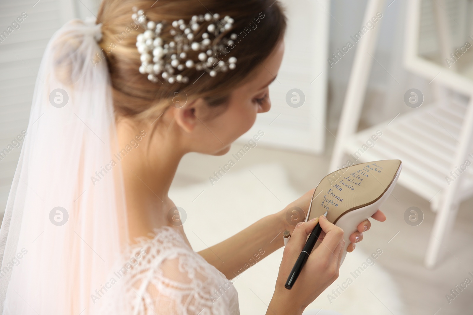 Photo of Young bride writing her single friends names on shoe indoors, closeup. Wedding superstition