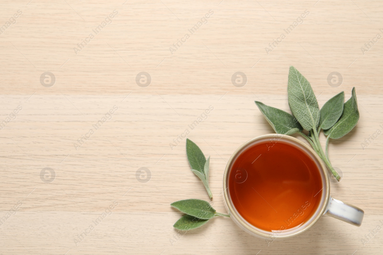 Photo of Cup of aromatic sage tea and fresh leaves on wooden table, flat lay. Space for text