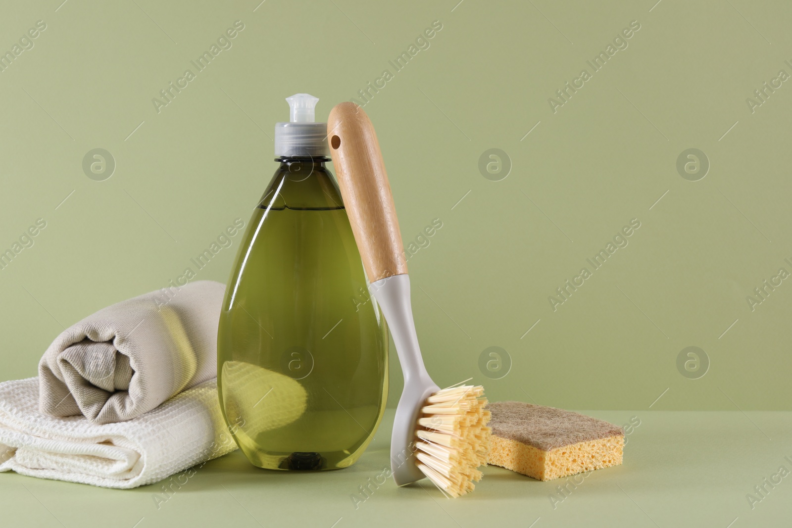 Photo of Bottle of cleaning product, sponge, rags and brush on light green background. Space for text