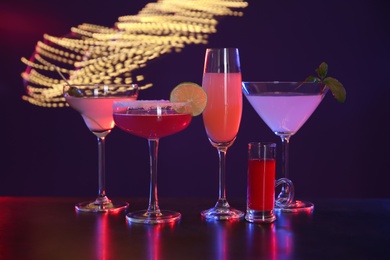 Photo of Many different alcoholic drinks on table against dark background with blurred lights