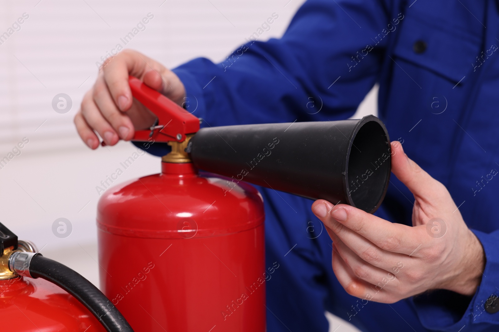 Photo of Man checking quality of fire extinguishers indoors, closeup