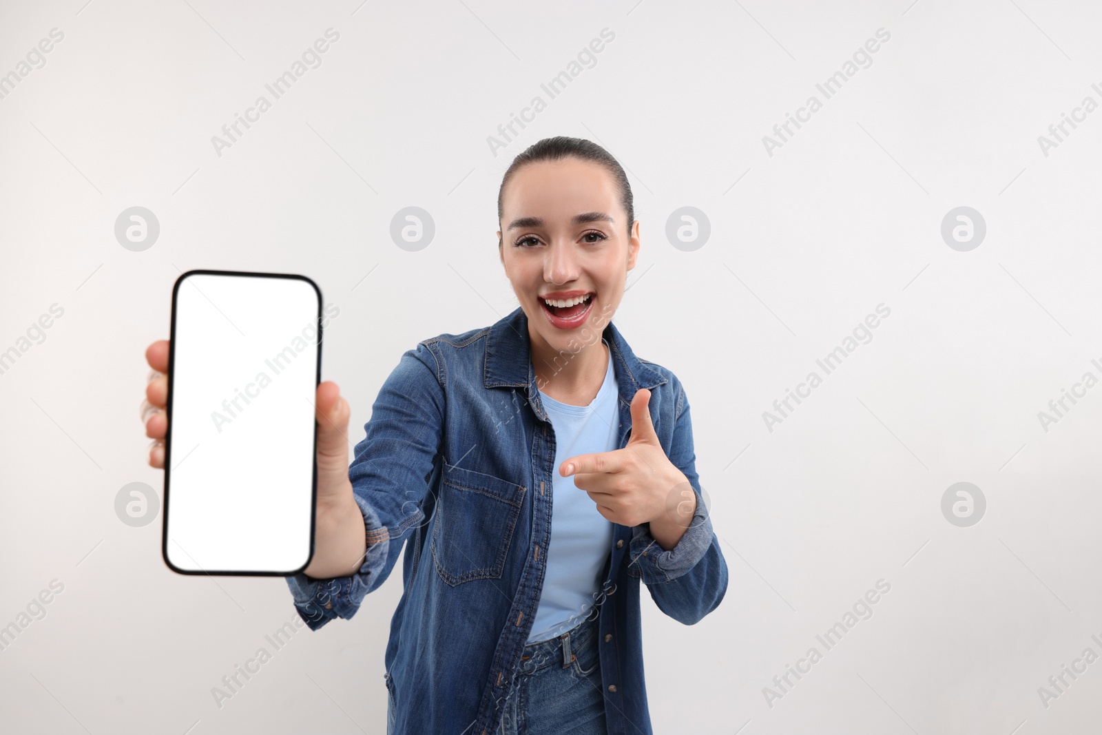 Photo of Young woman showing smartphone in hand and pointing at it on white background