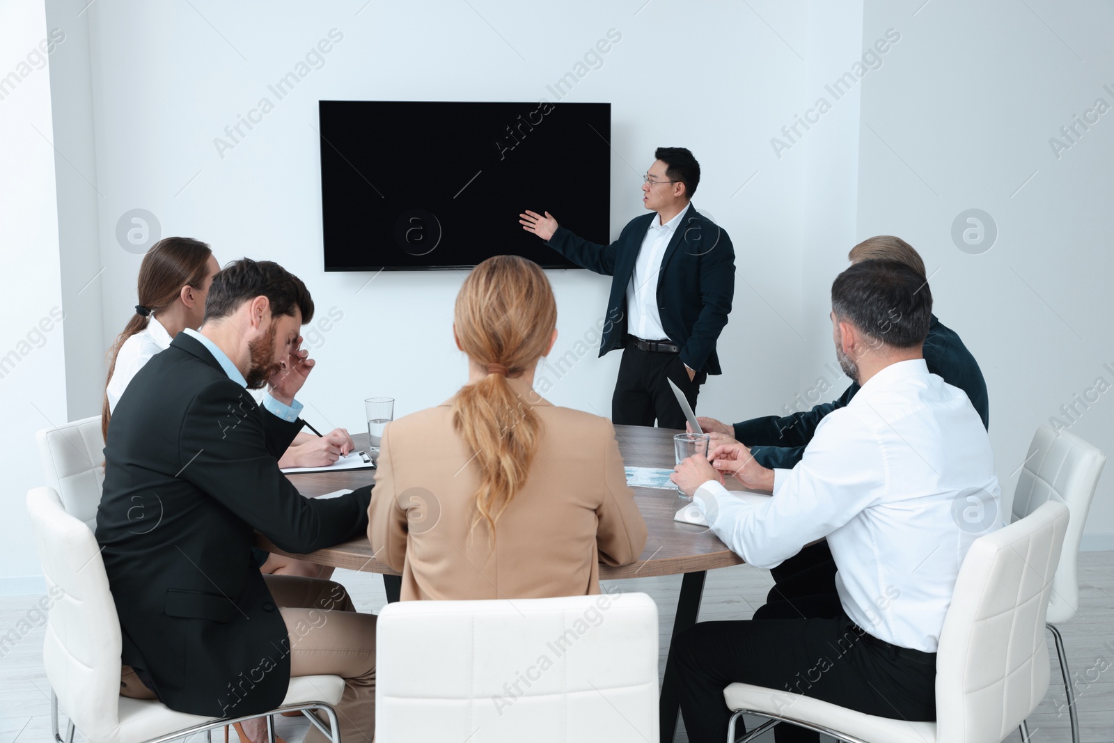 Photo of Business conference. Group of people listening to speaker report near tv screen in meeting room