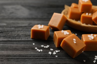 Photo of Yummy caramel candies and sea salt on black wooden table, , closeup. Space for text