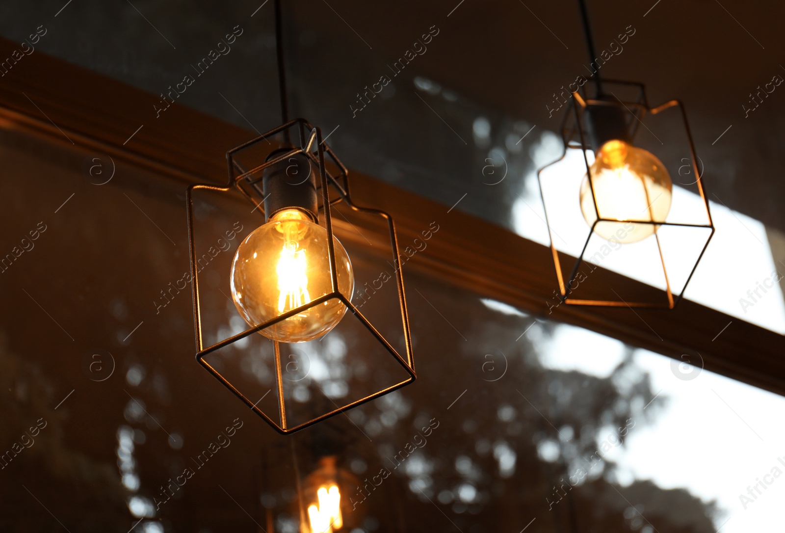 Photo of Pendant lamps with glowing light bulbs near window indoors