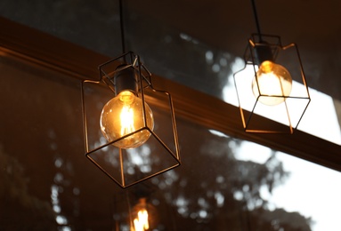 Photo of Pendant lamps with glowing light bulbs near window indoors