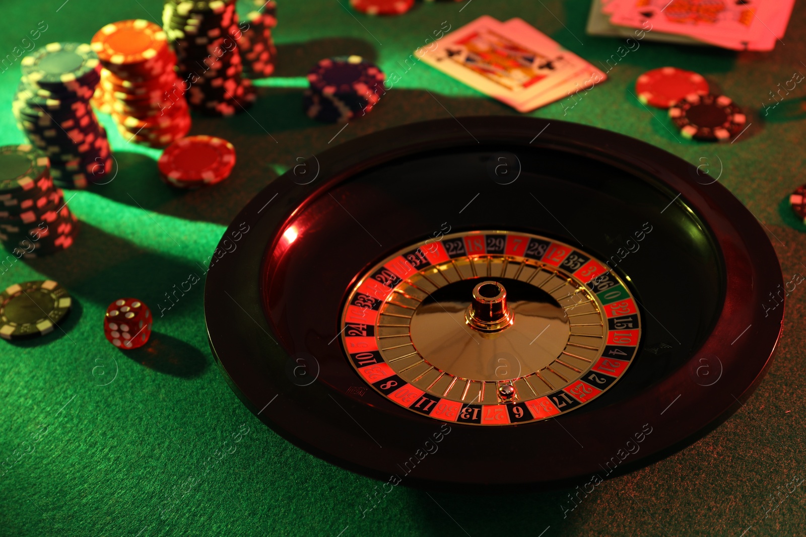 Photo of Roulette wheel with ball, playing cards and chips on green table. Casino game