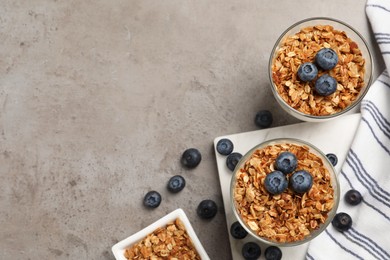 Glasses with granola and blueberries on grey table, flat lay. Space for text