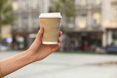 Photo of Woman holding paper takeaway cup on city street, closeup with space for text. Coffee to go