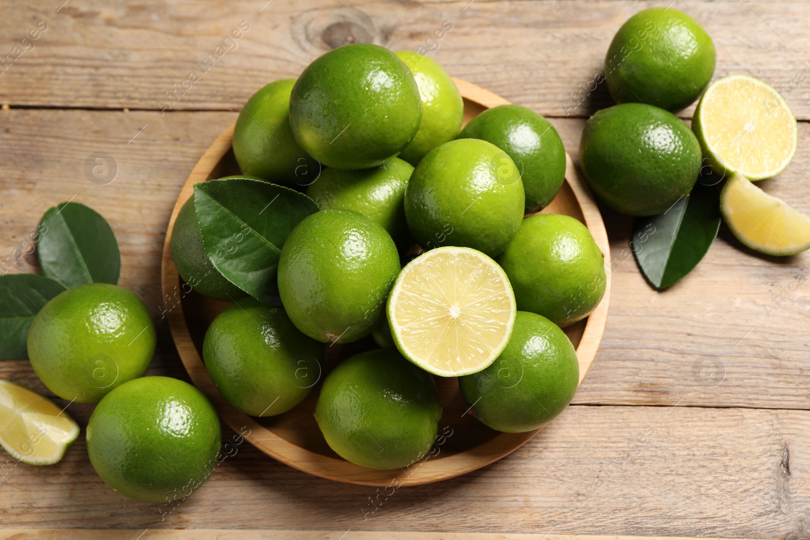 Photo of Fresh limes and green leaves on wooden table, flat lay