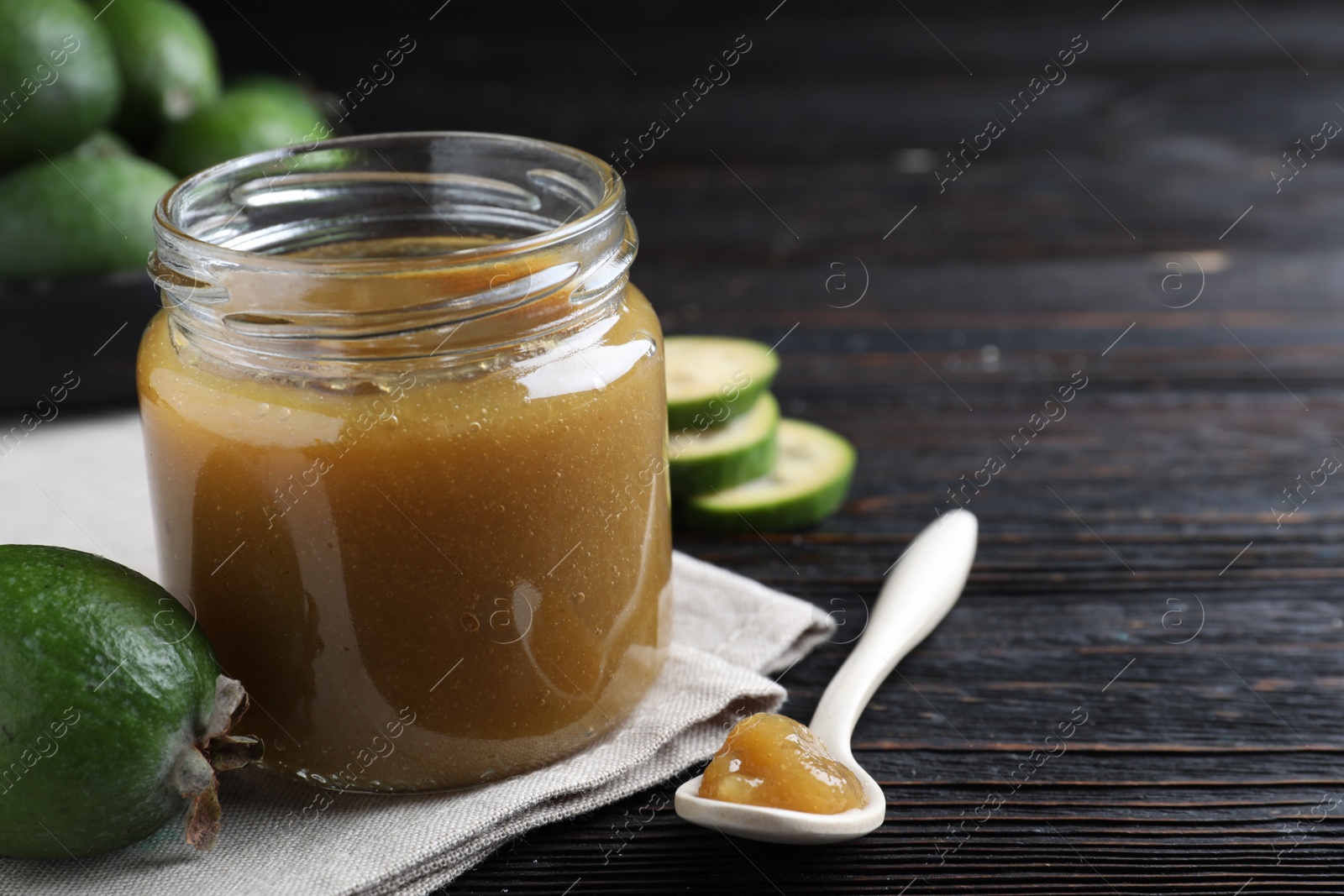 Photo of Feijoa jam and fresh fruit on black wooden table, closeup. Space for text