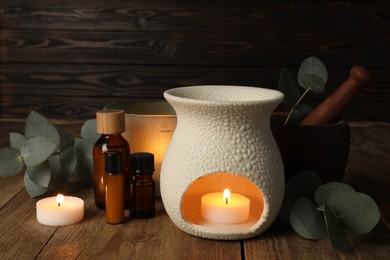Aromatherapy. Scented candles, bottles and eucalyptus branches on wooden table, closeup