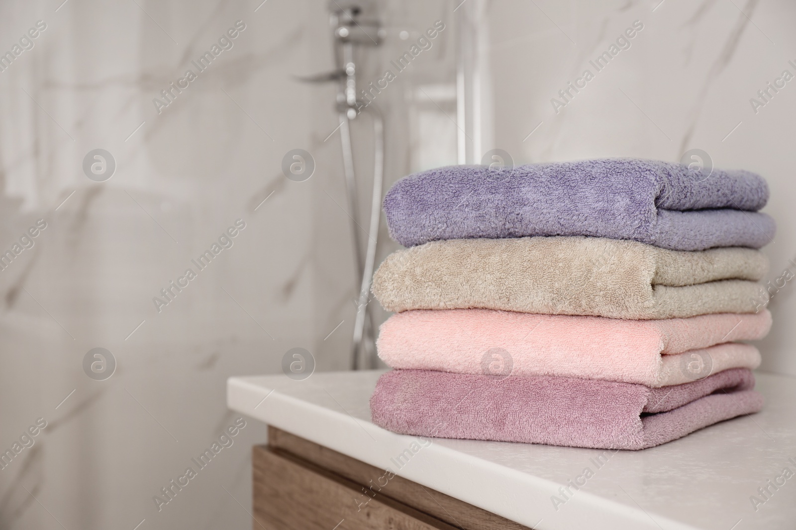 Photo of Stack of color towels on white table in bathroom. Space for text