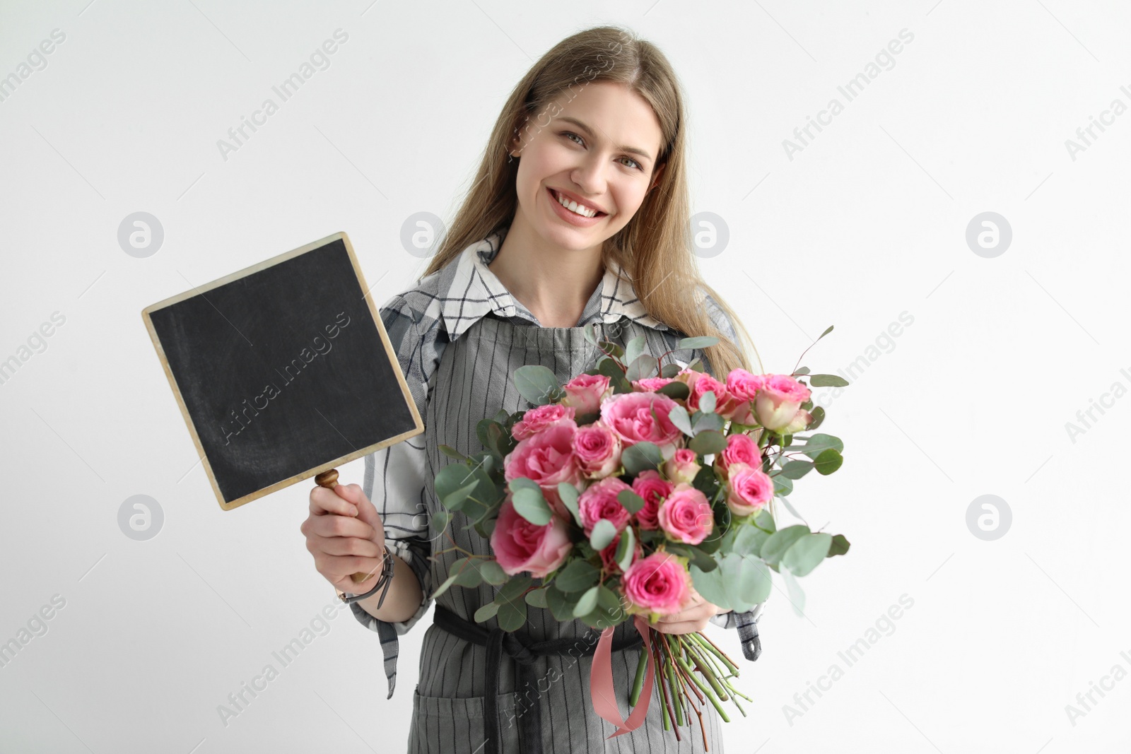 Photo of Female florist holding small chalkboard and bouquet on light background