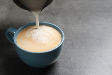 Pouring milk into cup of coffee on grey table, closeup. Space for text