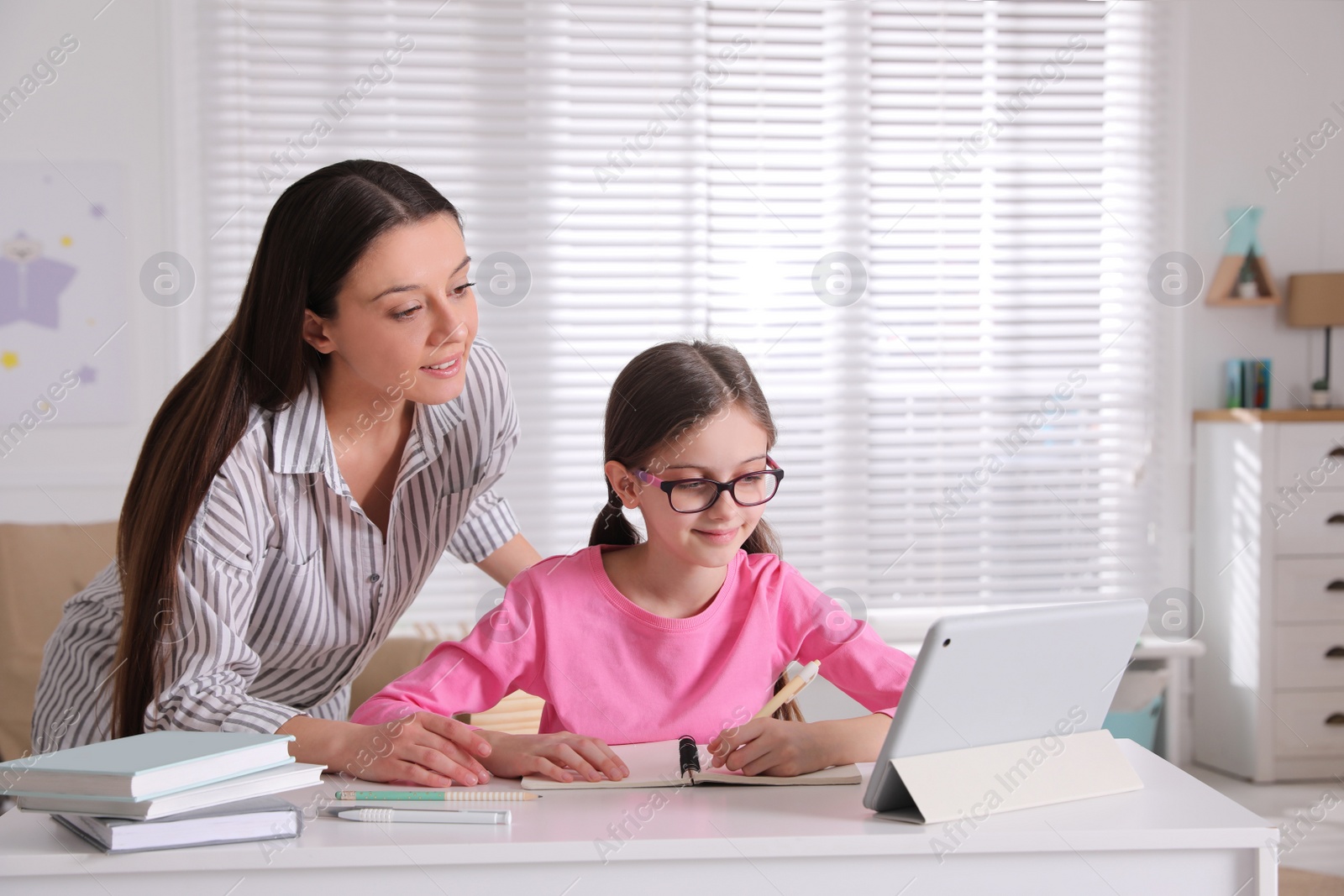 Photo of Mother helping her daughter doing homework with tablet at home